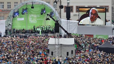 Papst Franziskus spricht am 25.05.2016 in einer Videobotschaft zur Eröffnung des Katholikentags in Leipzig zu einer Menschenmenge, die vor einer Bühne steht.