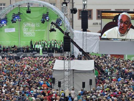 Papst Franziskus spricht am 25.05.2016 in einer Videobotschaft zur Eröffnung des Katholikentags in Leipzig zu einer Menschenmenge, die vor einer Bühne steht.
