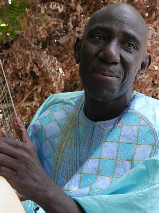 Der Musiker hält sein Instrument in der Hand, das aus einem halbkugeligen Körper besteht, auf dem ein Steg mehrere Saiten hält.