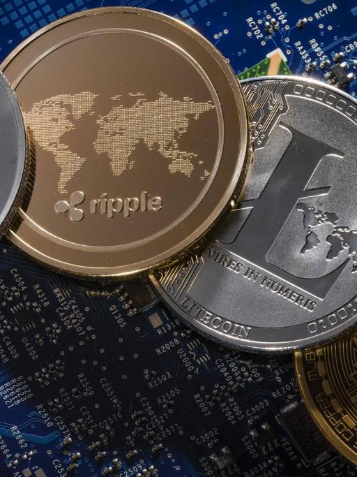 Münzen der Kryptowährungen Ethereum, ripple, Litecoin und Bitcoin liegen auf der Platine eines Computers