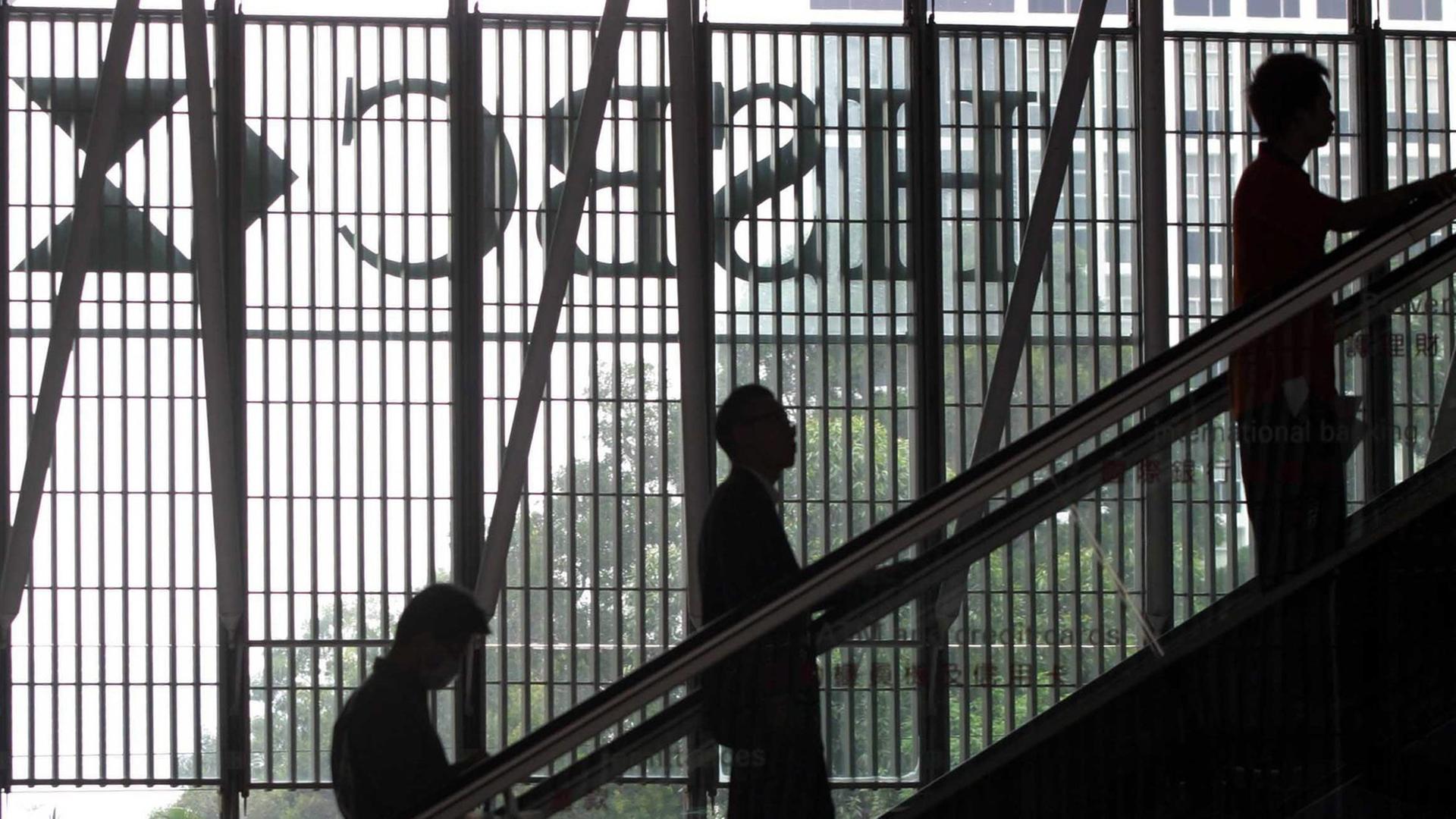 Menschen auf einer Rollstreppe, im Hintergrund das spiegelverkehrte Logo des HSBC-Bank. Menschen auf einer Rollstreppe, im Hintergrund das spiegelverkehrte Logo des HSBC-Bank.