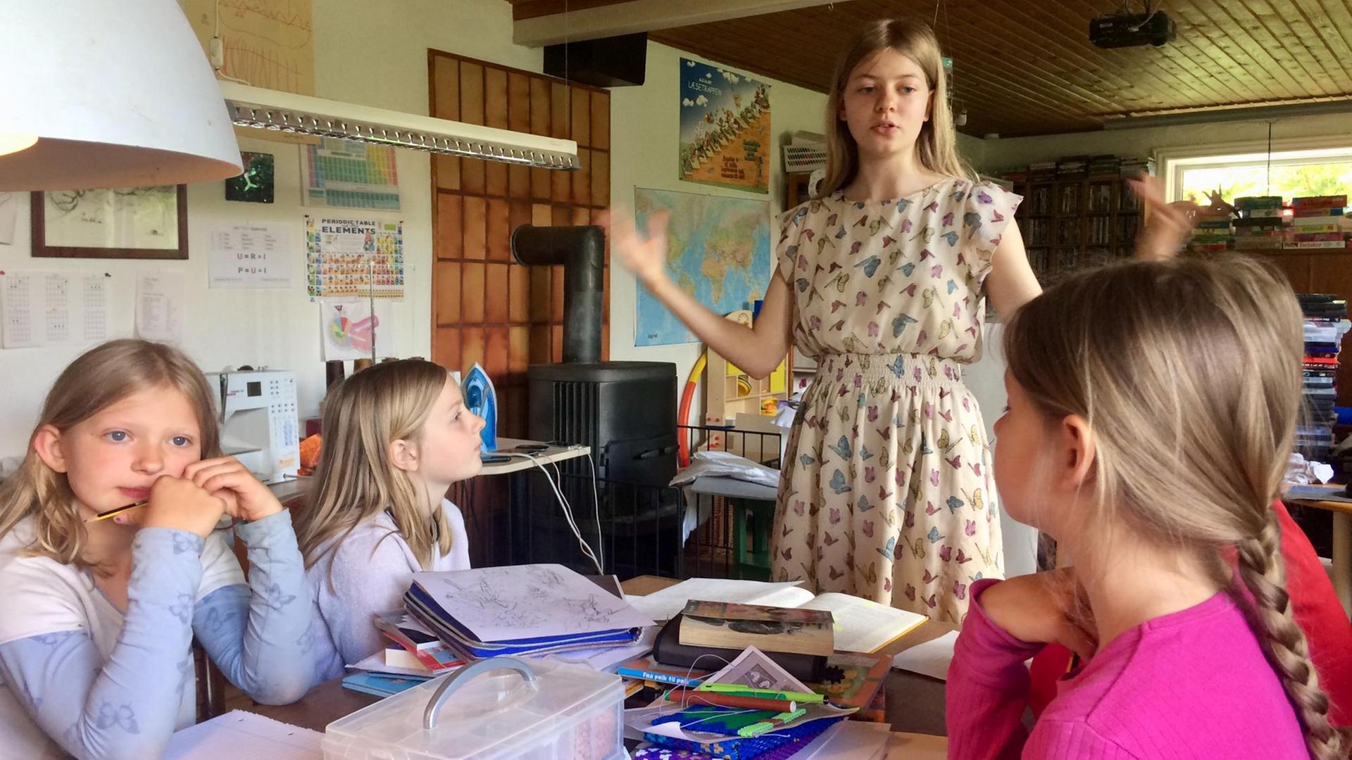 Ein Mädchen referiert stehend, vier weitere Kinder am Tisch sitzend hören ihr zu. Ein Mädchen referiert stehend, vier weitere Kinder am Tisch sitzend hören ihr zu.