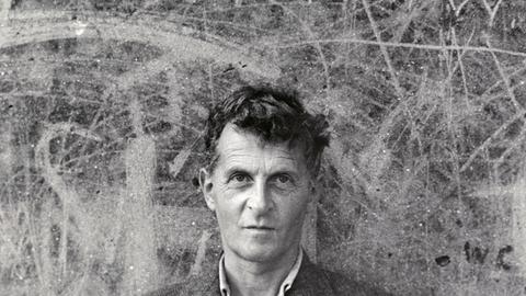 Schwarz-Weiß-Aufnahme von Ludwig Wittgenstein, vor einer zerkratzten Wand stehen.