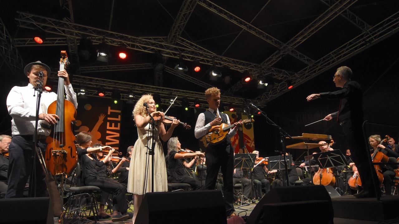 Drei Musiker mit großem Orchester stehen auf einer Bühne und spielen Musik. Drei Musiker mit großem Orchester stehen auf einer Bühne und spielen Musik.