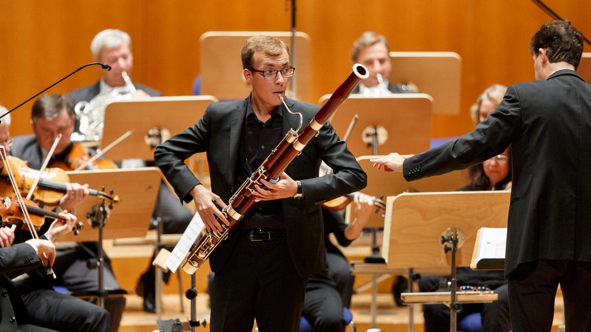 Ein junger Mann steht vor einem Orchester und spielt Fagott. Ein junger Mann steht vor einem Orchester und spielt Fagott.