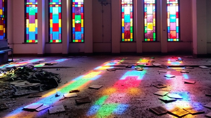 Sunbeams filter through the stained-glass windows of Mississippi University for Women's auditorium, creating colorful patterns on the stage, which is littered with broken glass.