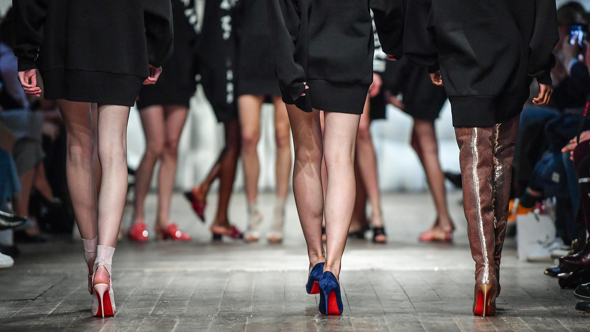 Drei Models auf dem Laufsteg, aufgenommen von hinten, man sieht ihre Beine, der Fokus liegt auf den Stöckelschuhen. Drei Models auf dem Laufsteg, aufgenommen von hinten, man sieht ihre Beine, der Fokus liegt auf den Stöckelschuhen.