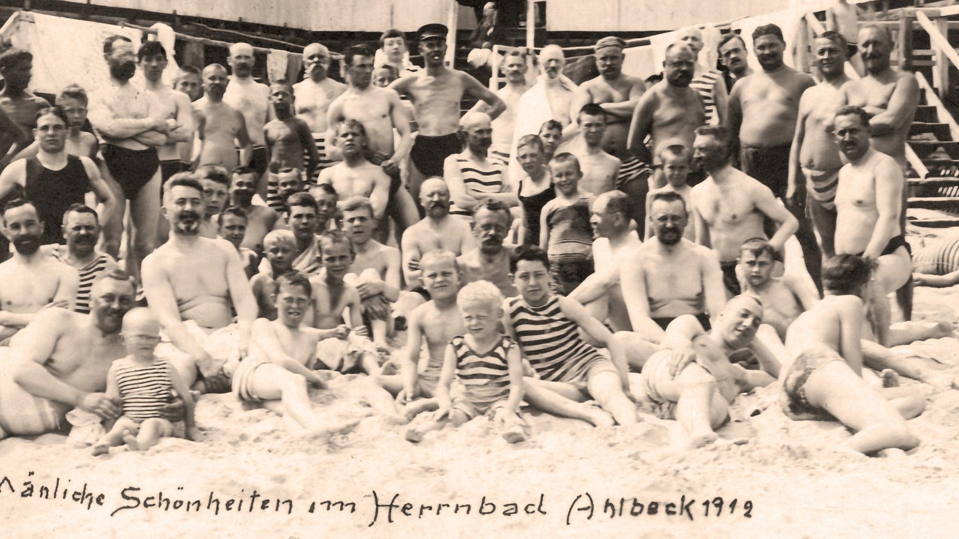 Die historische Fotografie mit dem Schriftzug "Mänliche Schönheiten im Herrenbad Ahlbeck 1912" aus dem Jahr 1912 zeigt Männer und Kinder im Herrenbad von Ahlbeck, Ostseebad, auf der Insel Usedom.