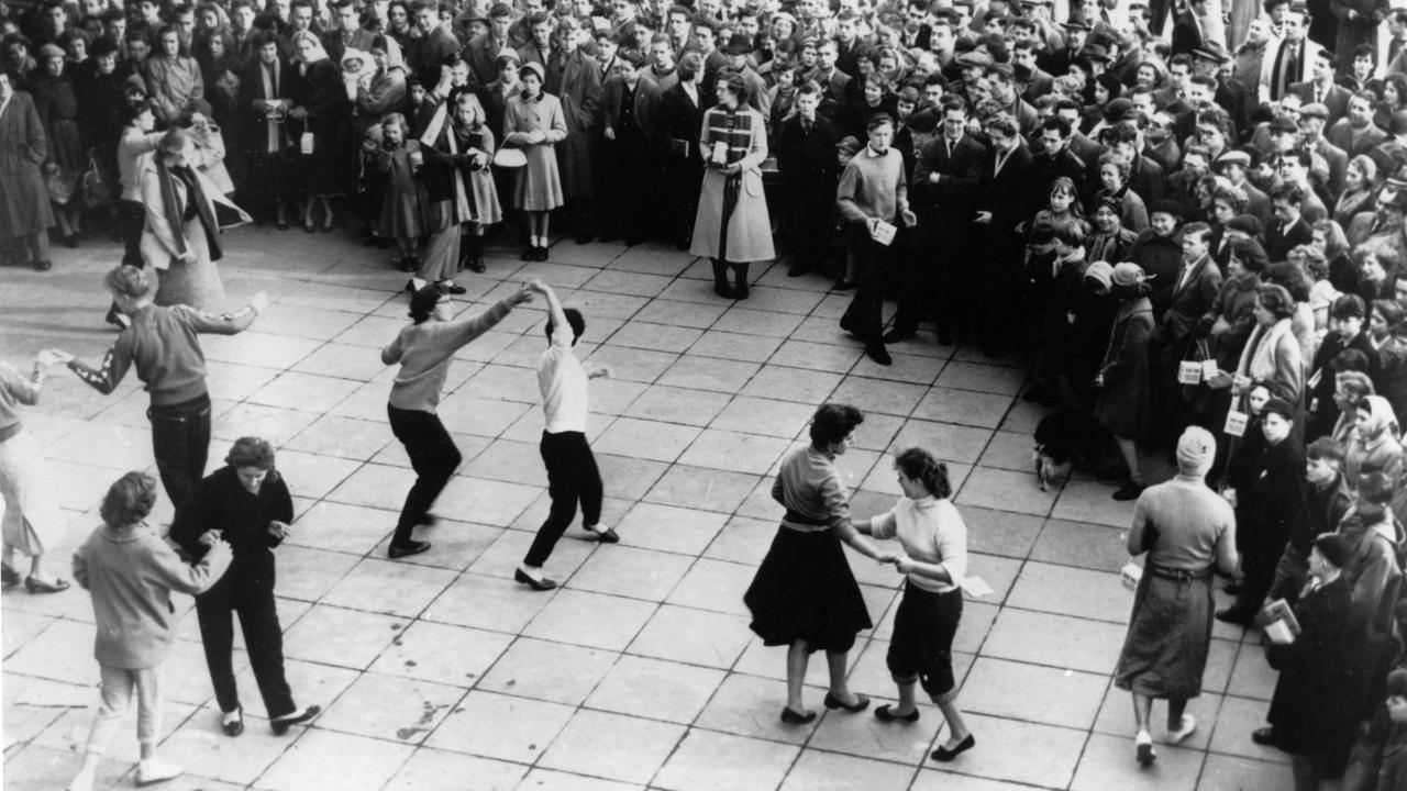 Paare tanzen auf einem Platz im Freien umgeben von einer Menschenmengen.