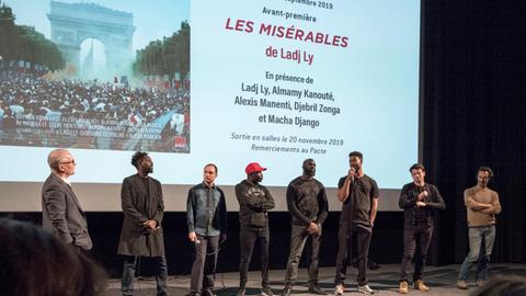 Der französische Filmemacher Ladj Ly (2.v.l.) stellt zusammen mit der Filmcrew seinen Film "Les Miserables" im September 2019 in Lyon vor. Mehrere Männer stehen in einem Kino vor der Leinwand.