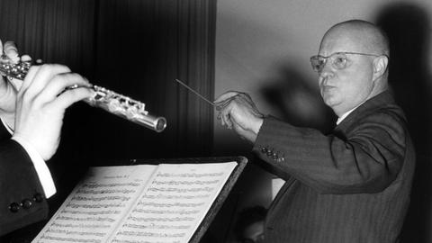 Der deutsche Komponist und Dirigent Paul Hindemith bei einer Orchesterprobe, bei der er mit einem Flötisten in Blickkontakt steht.