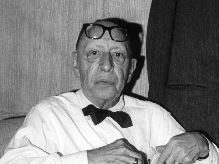 Der Komponist Igor Strawinsky mit weißem Hemd, schwarzer Fliege und einer Brille auf der Stirn.