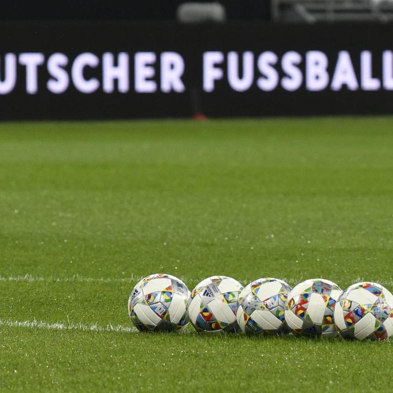 Mehrere Fussbälle liegen aufgereiht auf dem Rasen, im Hintergrund eine Bandenwerbung mit Logo und Schriftzug "Deutscher Fussball-Bund" 