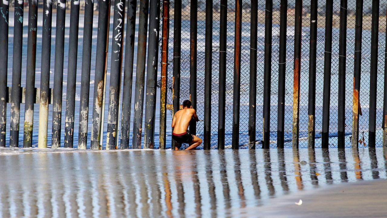 Ein Mann späht am 10.11.2016 am Strand von Tijuana durch den Grenzzaun zwischen Mexiko und den USA