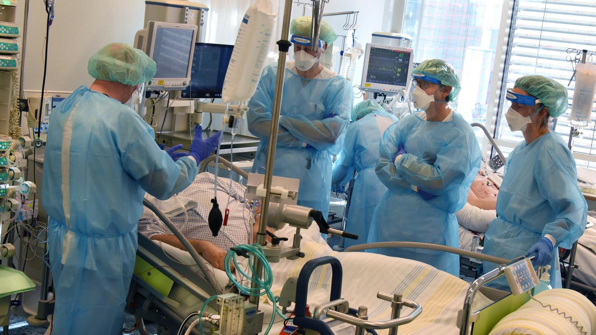 Mehrere Ärzte stehen in Schutzkleidung am Bett eines Intensivpatienten Mehrere Ärzte stehen in Schutzkleidung am Bett eines Intensivpatienten