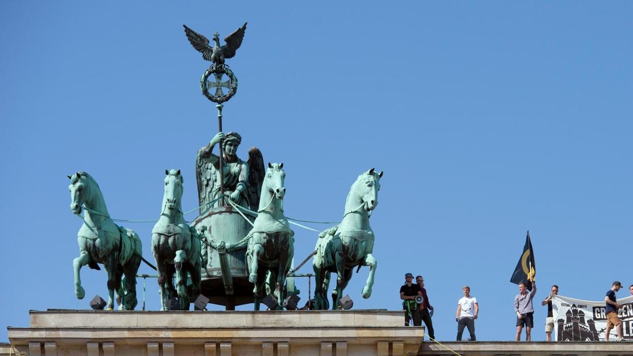 Aktivisten der "Identitaeren Bewegung" stehen neben der Quadriga auf dem Brandenburger Tor und zeigen ein Transparent. Aktivisten der "Identitaeren Bewegung" stehen neben der Quadriga auf dem Brandenburger Tor und zeigen ein Transparent.