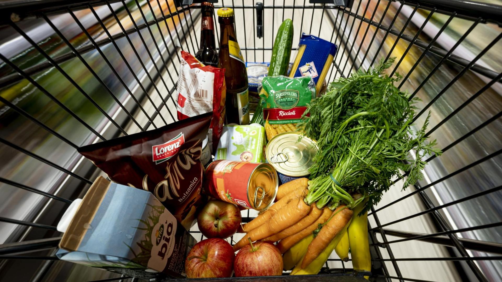 Gemüse und andere Produkte liegen in einem Einkaufswagen in einem Supermarkt. Der Wagen ist von oben und mit einem fischauge-ähnlichen Effekt zu sehen. Gemüse und andere Produkte liegen in einem Einkaufswagen in einem Supermarkt. Der Wagen ist von oben und mit einem fischauge-ähnlichen Effekt zu sehen.