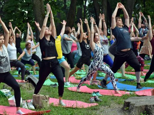Das Bild zeigt eine Yoga-Gruppe, die unter freiem Himmel Übungen macht.