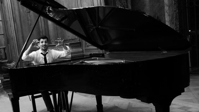 Der englische Pianist Hector Docx sitzt mit erhobenen Händen an einem Flügel