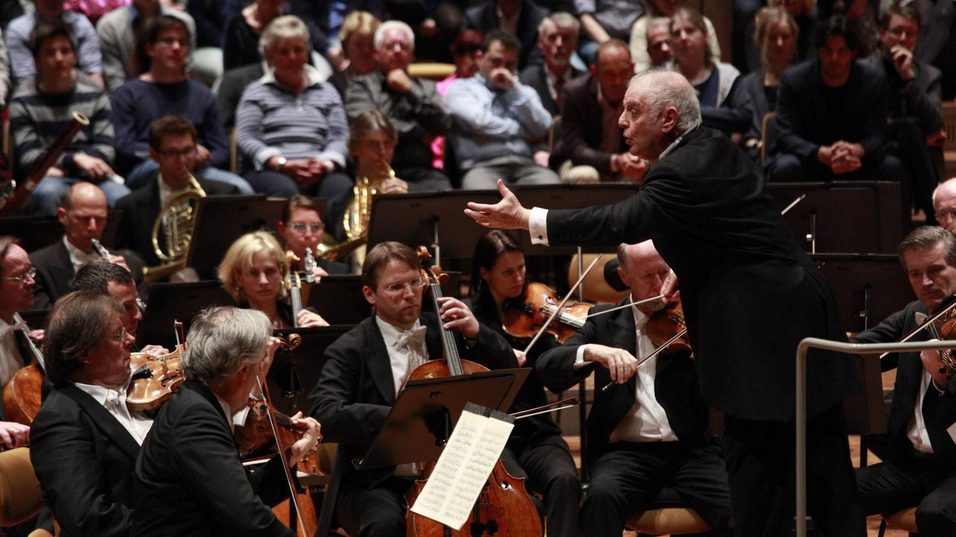 Daniel Barenboim mit einer ausladenden Geste vor dem Orchester, im Hinergrund ist Publikum zu sehen. Daniel Barenboim mit einer ausladenden Geste vor dem Orchester, im Hinergrund ist Publikum zu sehen.