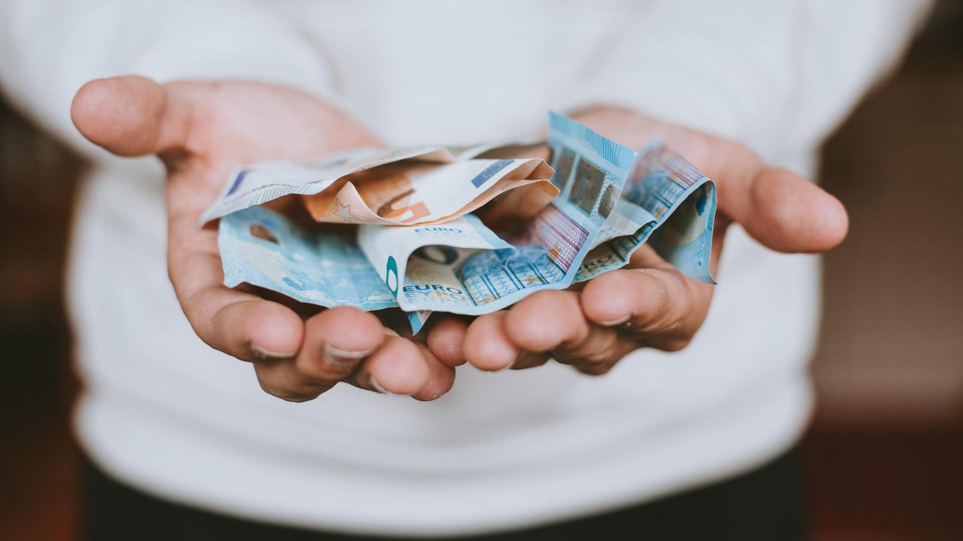 Zwei ausgestreckte Hände halten zerknitterte Euroscheine. Zwei ausgestreckte Hände halten zerknitterte Euroscheine.