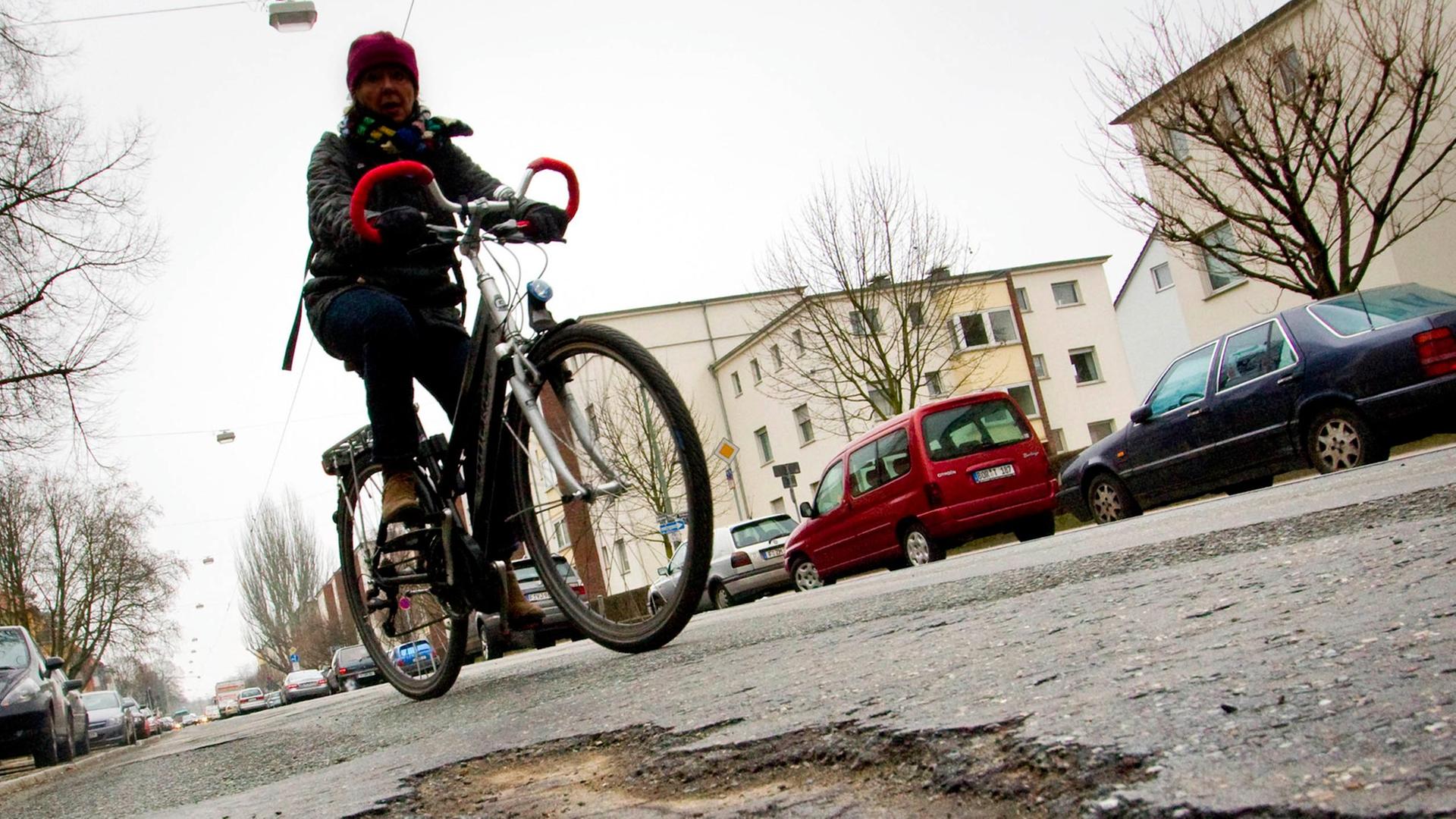 Eine Radfahrerin rollt am Montag (08.02.2010) auf dem Marbachweg in Frankfurt am Main an einem Schlagloch vorbei. Eine Radfahrerin rollt am Montag (08.02.2010) auf dem Marbachweg in Frankfurt am Main an einem Schlagloch vorbei.