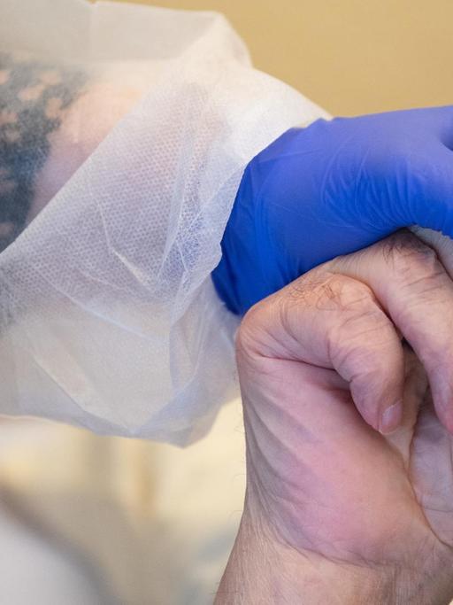 18.11.2020, Baden-Württemberg, Tübingen: Eine Altenpflegerin in Schutzausrüstunghält die Hand eines Bewohners. Foto: Sebastian Gollnow/dpa | Verwendung weltweit