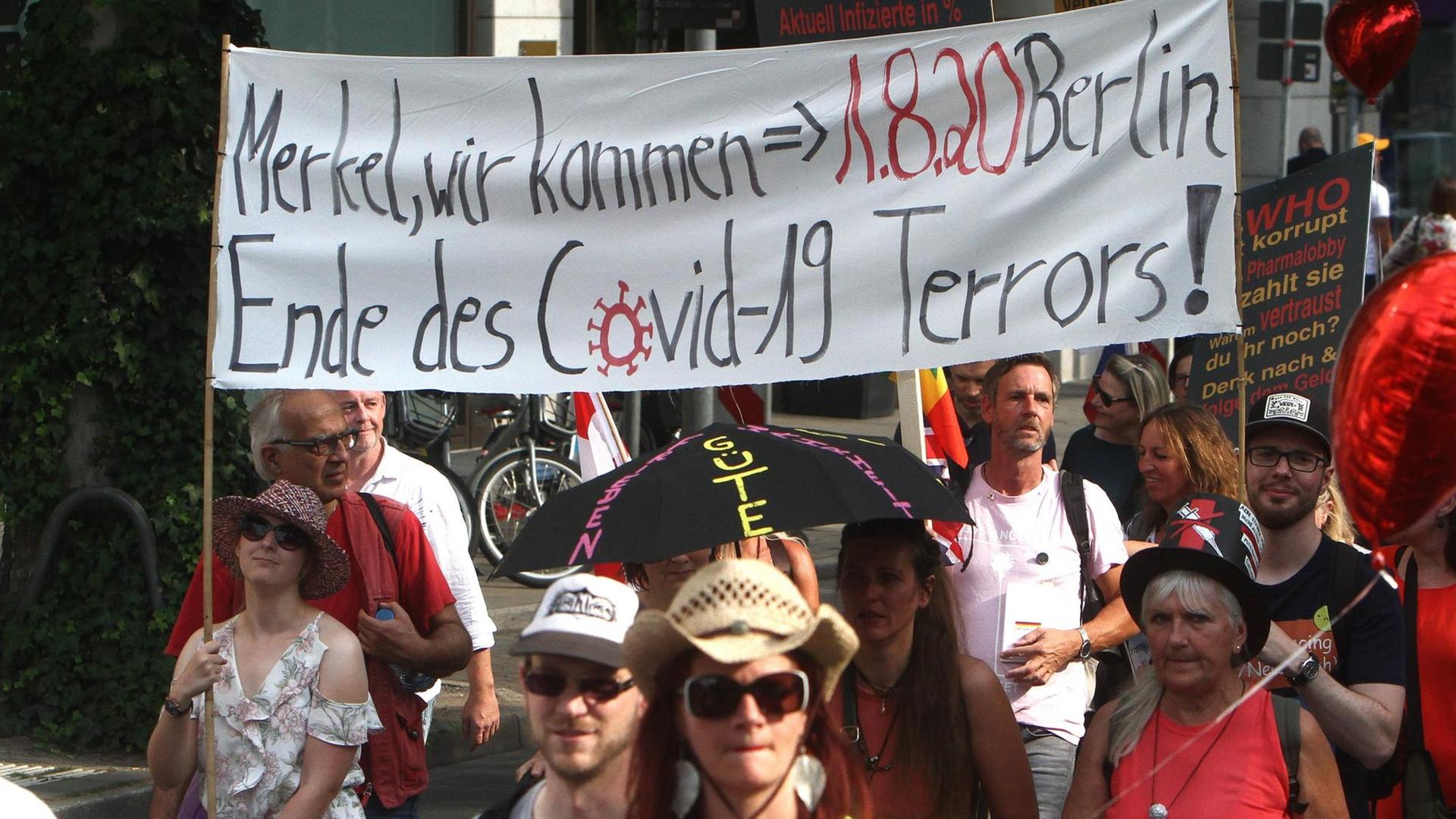 Demonstranten tragen ein weißes Stoffbanner, auf dem steht: "Merkel wir kommen - 1.8.20 Berlin - Ende des Covid-19-Terrors" Demonstranten tragen ein weißes Stoffbanner, auf dem steht: "Merkel wir kommen - 1.8.20 Berlin - Ende des Covid-19-Terrors"