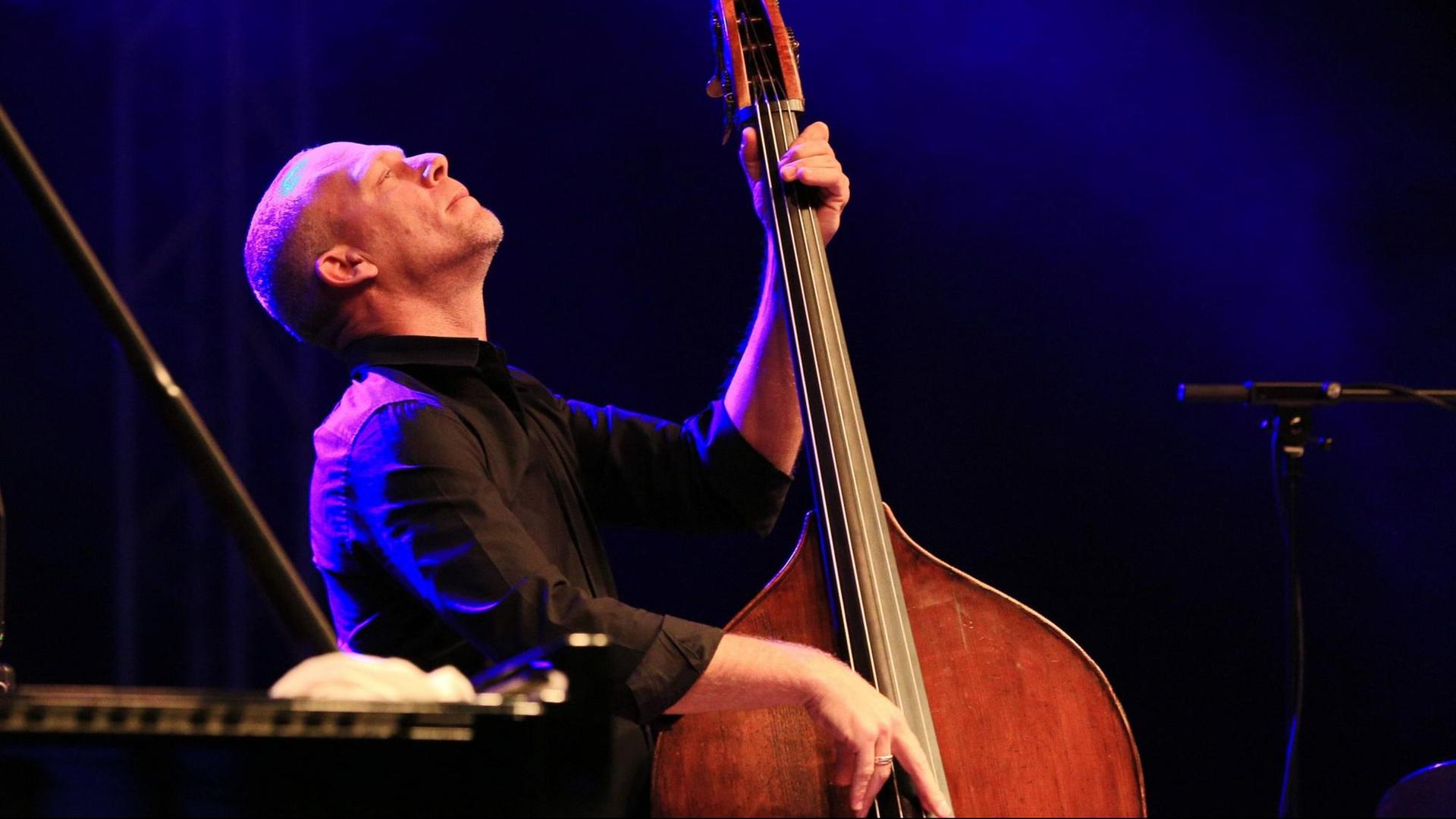 Der Komponist, Sänger und Kontrabassist Avishai Cohen legt beim Spiel auf einer bunt beleuchteten Bühne seinen Kopf in den Nacken, die Augen geschlossen, während er den Kontrabass hält und zupft. Der Komponist, Sänger und Kontrabassist Avishai Cohen legt beim Spiel auf einer bunt beleuchteten Bühne seinen Kopf in den Nacken, die Augen geschlossen, während er den Kontrabass hält und zupft.
