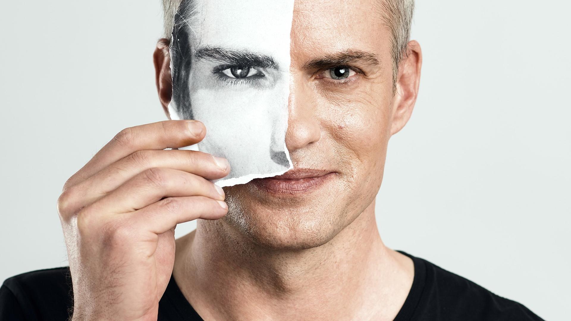 Close-Up-Porträt von Florian Burkhardt. Er hält sich das identische Bild in schwarz-weiß und angerissenem Papier vor die rechte Gesichtshälfte.