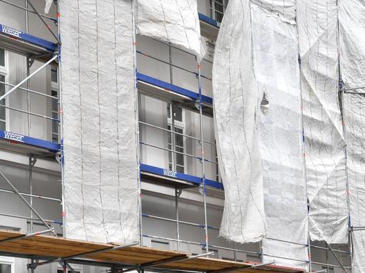 Ein Haus in München ist eingerüstet, am Gerüst hängen Planen und verdecken die Fassade zum Teil.