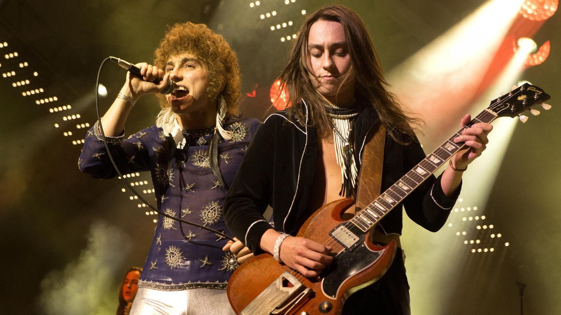 Zwei Männer stehen auf einer Bühne. Der Mann links hält ein Mikrofon in der Hand und singt. Der Mann rechts spielt Gitarre. Zwei Männer stehen auf einer Bühne. Der Mann links hält ein Mikrofon in der Hand und singt. Der Mann rechts spielt Gitarre.