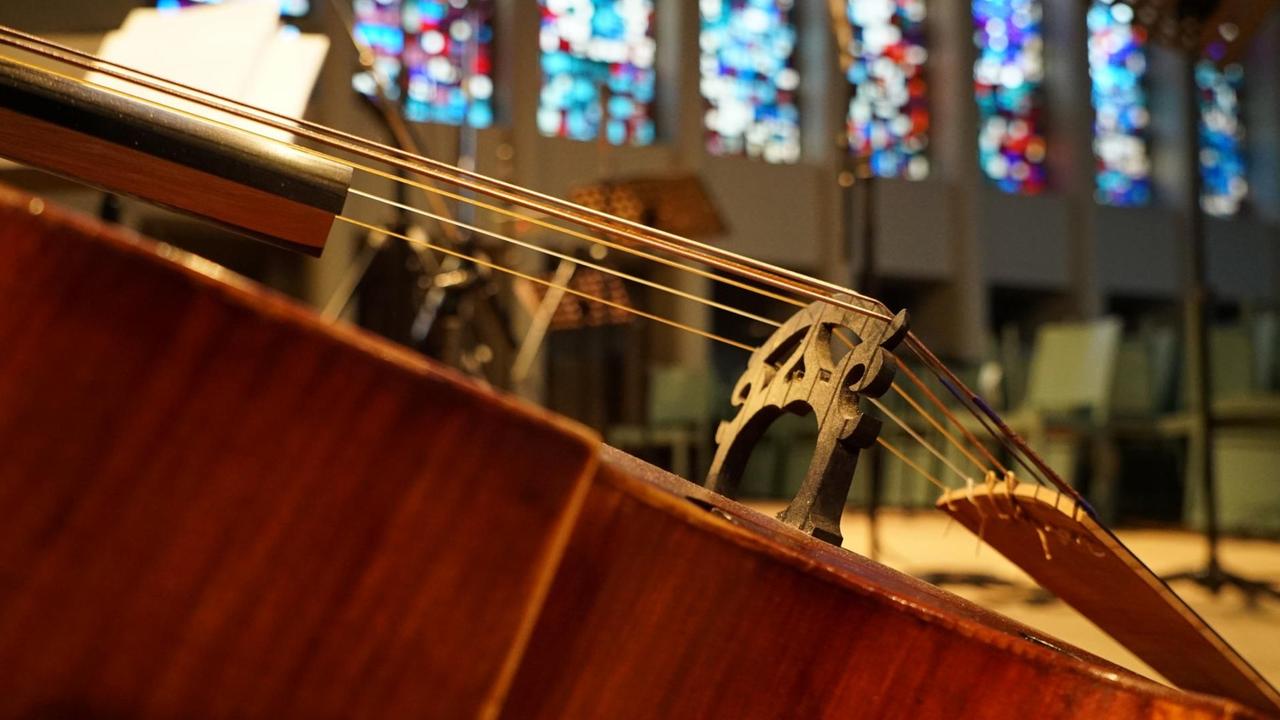 Ein großes Streichinstrument lehnt an einem Stuhl, dahinter bunte Kirchenfenster. Ein großes Streichinstrument lehnt an einem Stuhl, dahinter bunte Kirchenfenster.