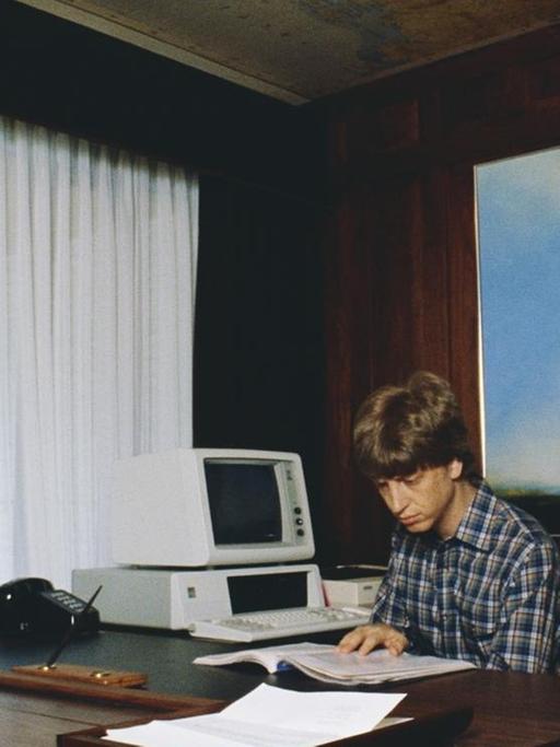 Microsoft Co-Gründer Bill Gates sitzt an einem großen Schreibtisch in seinem zuhause.