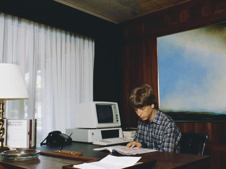 Microsoft Co-Gründer Bill Gates sitzt an einem großen Schreibtisch in seinem zuhause.