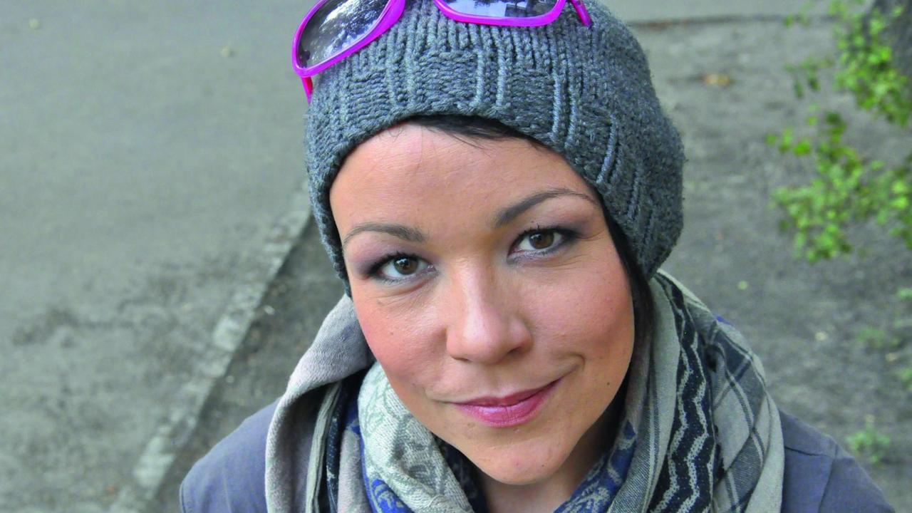 Winnie Brückner lächelt nach oben in die Kamera. Sie trägt eine graue Wollmütze auf der eine lilafarbene Brille steckt. Winnie Brückner lächelt nach oben in die Kamera. Sie trägt eine graue Wollmütze auf der eine lilafarbene Brille steckt.