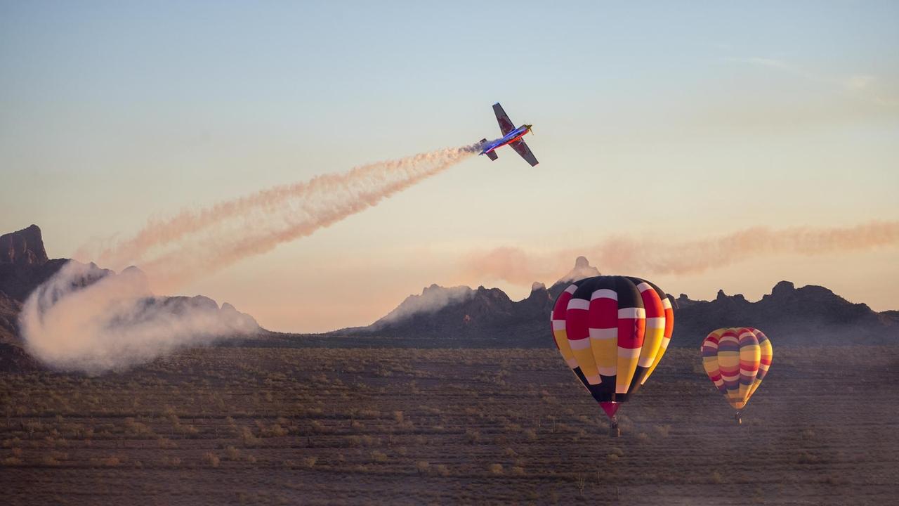 Ein kleines Flugzeug mit Red Bull-Logo dreht kurz vor zwei Heißluftballons ab.