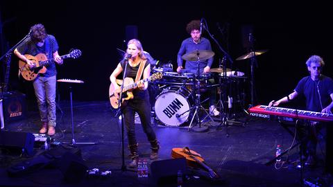 Die Sängerin Dota mit Gitarre am Mikrofon auf der Bühne des Theaterkahns in Dresden umgeben von drei Musikern der Band Dota an Keyboard, Schlagzeug und E-Gitarre