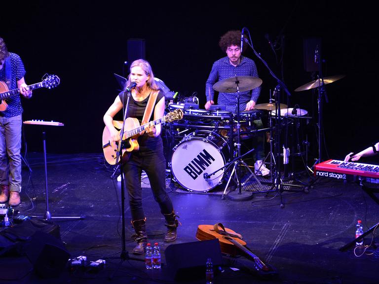 Die Sängerin Dota mit Gitarre am Mikrofon auf der Bühne des Theaterkahns in Dresden umgeben von drei Musikern der Band Dota an Keyboard, Schlagzeug und E-Gitarre