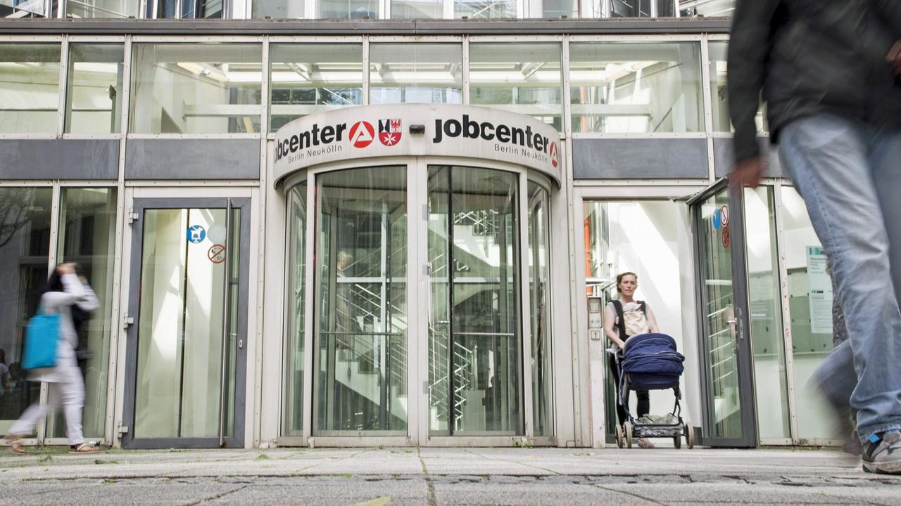 Vor der Drehtür des Eingang des Jobcenters in Berlin Neukölln sind Menschen zu sehen. Vor der Drehtür des Eingang des Jobcenters in Berlin Neukölln sind Menschen zu sehen.