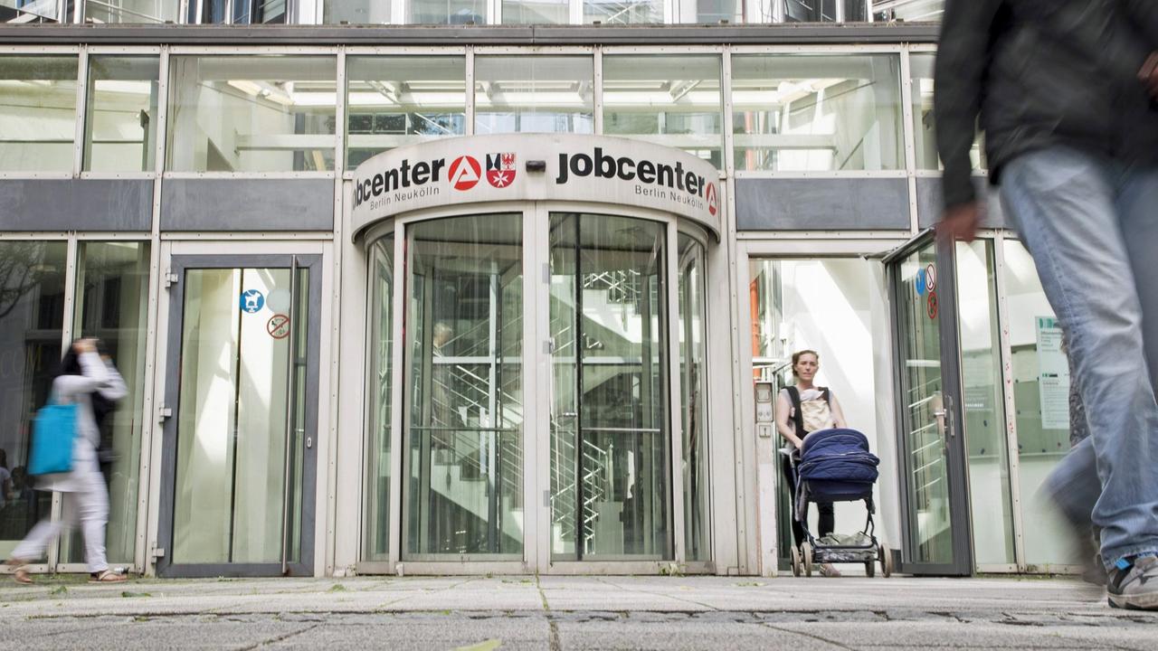 Vor der Drehtür des Eingang des Jobcenters in Berlin Neukölln sind Menschen zu sehen. Vor der Drehtür des Eingang des Jobcenters in Berlin Neukölln sind Menschen zu sehen.
