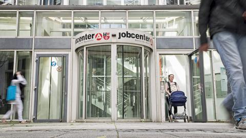 Vor der Drehtür des Eingang des Jobcenters in Berlin Neukölln sind Menschen zu sehen.