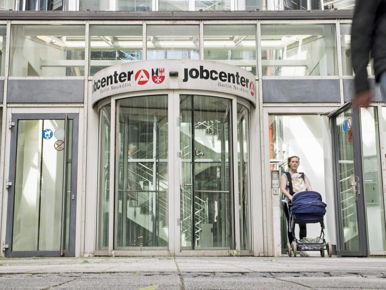 Vor der Drehtür des Eingang des Jobcenters in Berlin Neukölln sind Menschen zu sehen.