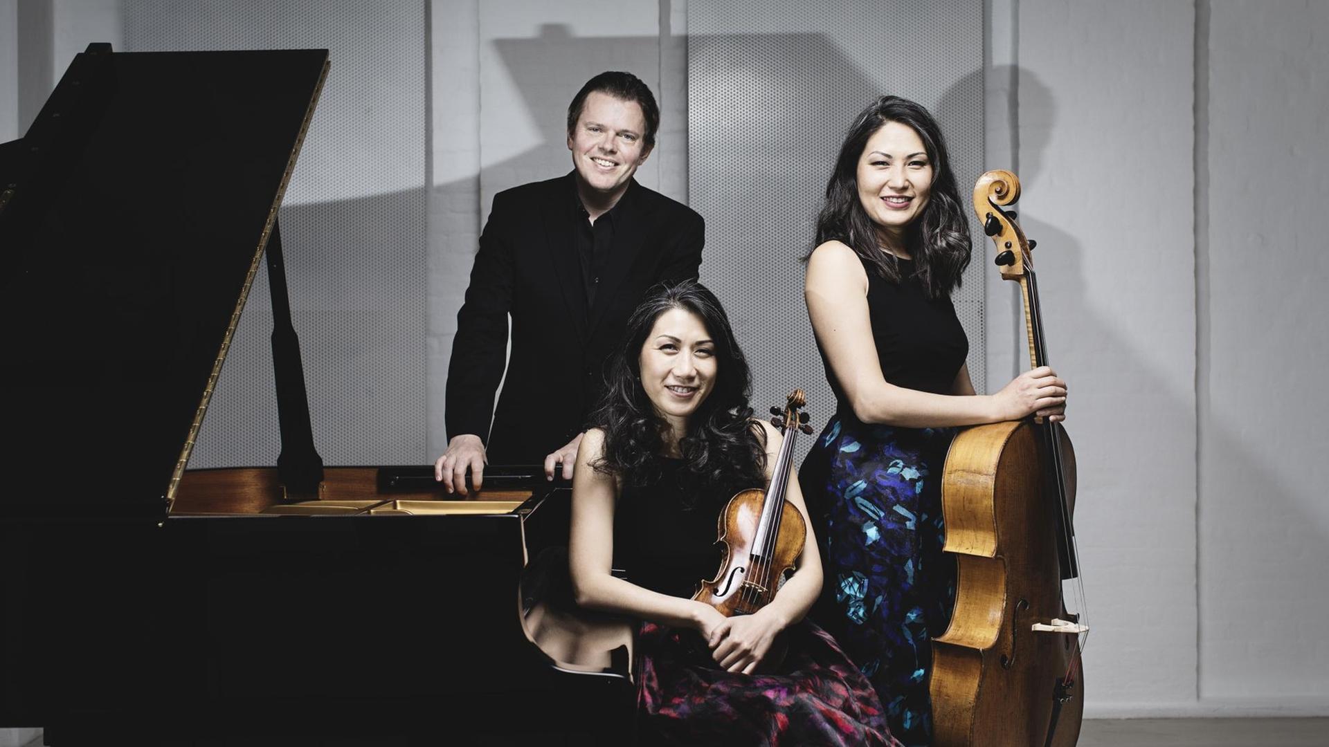 Das Mitglieder des Trio con Brio Copenhagen stehen und sitzen an einem Flügel und lächeln in die Kamera. Das Mitglieder des Trio con Brio Copenhagen stehen und sitzen an einem Flügel und lächeln in die Kamera.