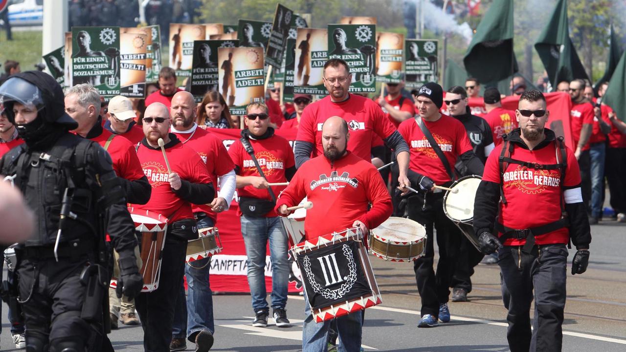 Mehrere Mitglieder der rechtsextremen Partei Der Dritte Weg sind zu sehen, wie sie Trommeln tragen unter hinter einem Polizisten hergehen. Sie tragen die Farben des Deutschen Reichs: Rot, schwarz und weiß Mehrere Mitglieder der rechtsextremen Partei Der Dritte Weg sind zu sehen, wie sie Trommeln tragen unter hinter einem Polizisten hergehen. Sie tragen die Farben des Deutschen Reichs: Rot, schwarz und weiß