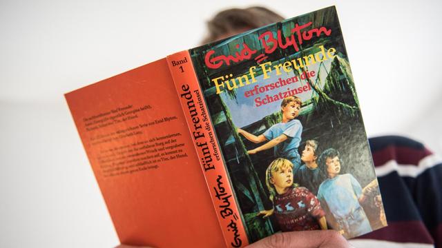 Ein Mann hält den ersten Band der Abenteuerserie "Fünf Freunde" von Schriftstellerin Enid Blyton in der Hand.