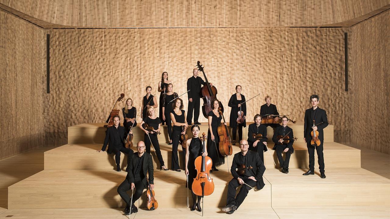 Rund 20 Menschen stehen mit ihren Instrumenten in einem hellbraunen Raum, es ist der kleine Saal der Elbphilharmonie in Hamburg.