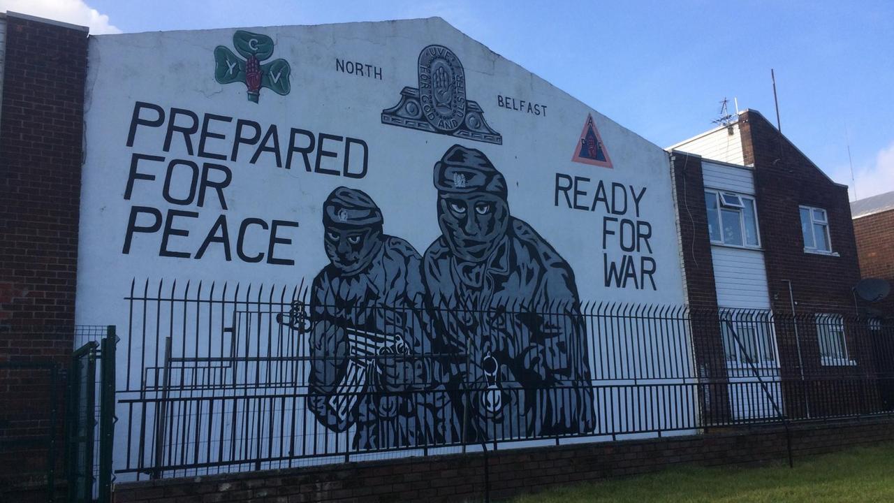 Wandgemälde im Norden von Belfast: Zwei vermummte Männer mit Gewehren, neben ihnen die Worte „Auf Frieden vorbereitet. Zum Krieg bereit.“ 
