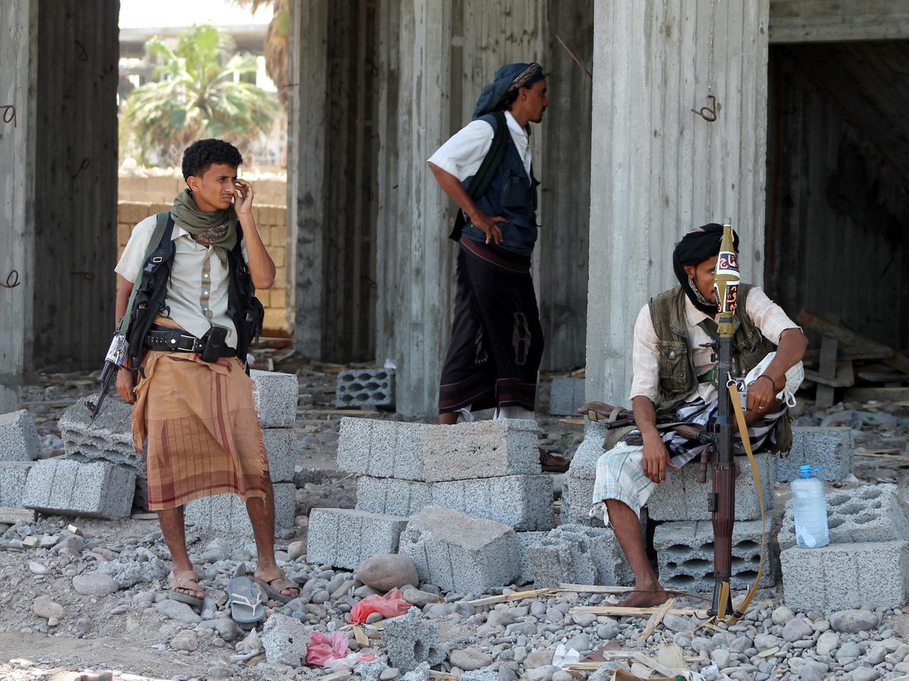 Bewaffnete Kämpfer stehen und sitzen nahe der jemenitischen Stadt Aden auf Trümmern.