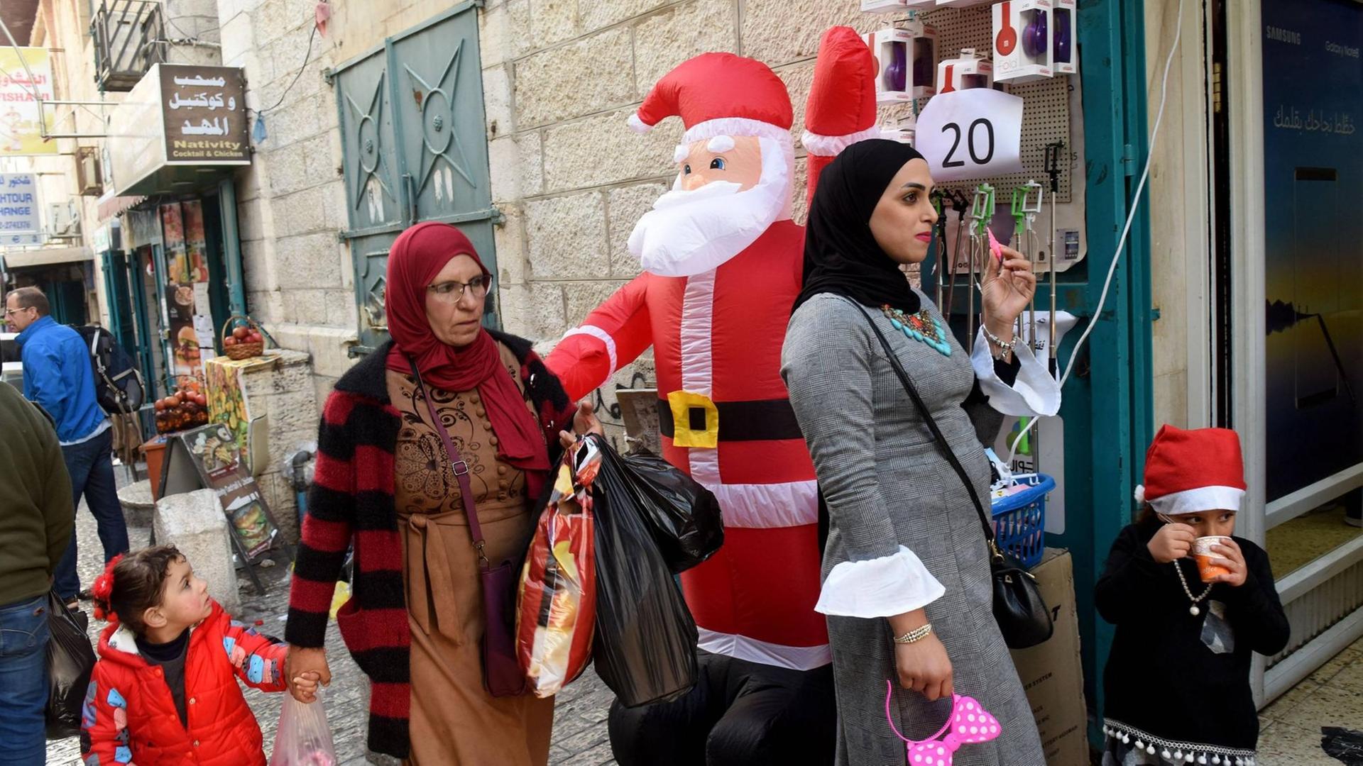Passanten stehen vor einem Laden mit einem aufblasbaren Weihnachtsmann in Bethlehem